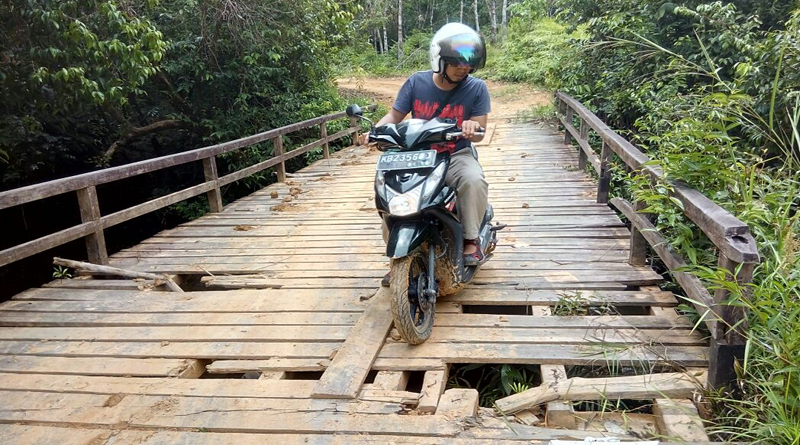 Seorang-warga-ketika-melintasi-jembatan-Sungai-Sebaju-yang-sudah-banyak-berlubang-pada-bagian-lantainya